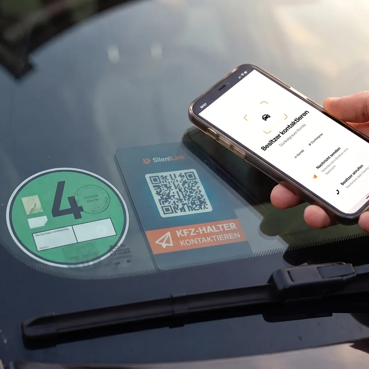 Eine Hand hält ein Handy mit der Seite Besitzer kontaktieren vor die Windschutzscheibe, dahinter die DriveID neben der Umweltplakette