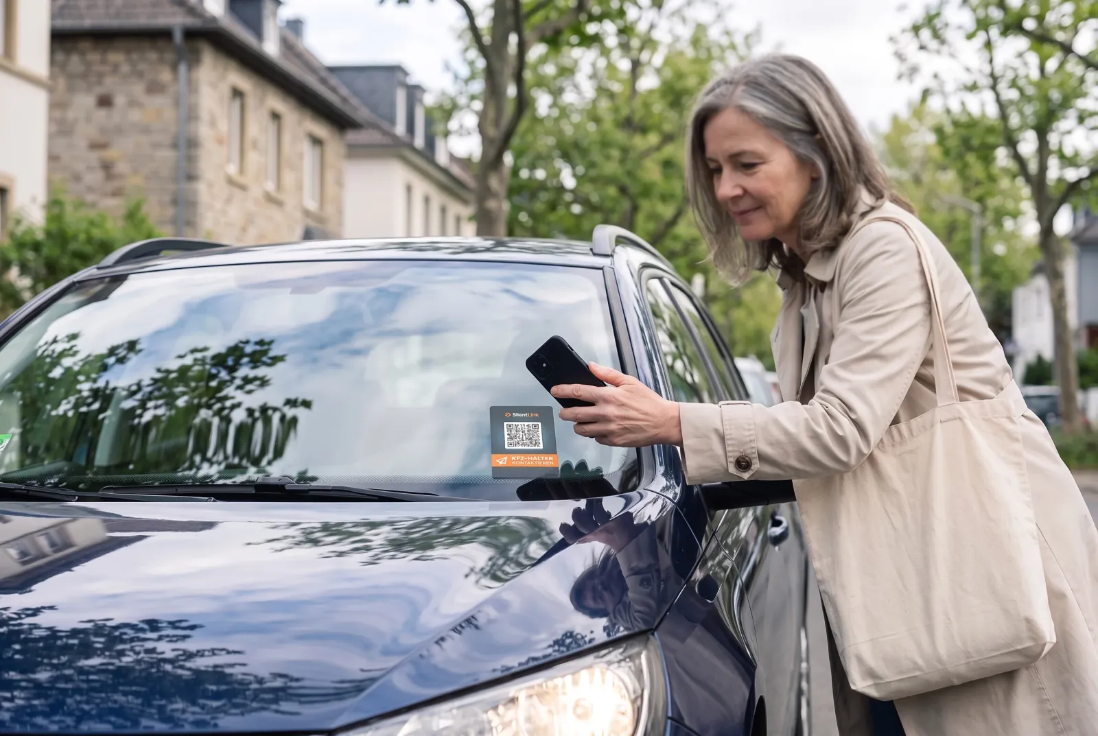Eine Frau hält ihr Handy vor die Windschutzscheibe eines geparkten Autos, hinter der die DriveID klebt