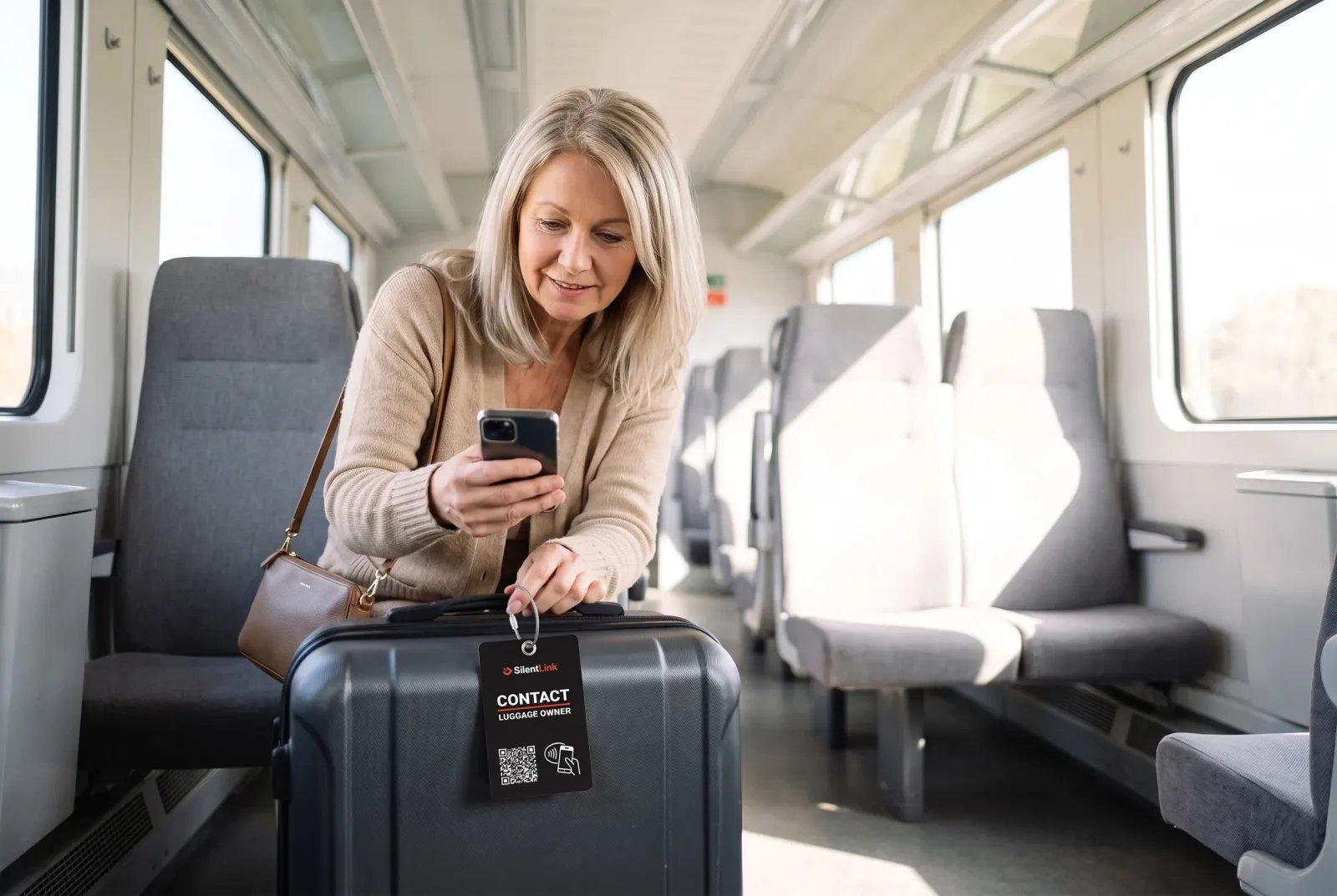 Eine Frau hat im Zug einen liegengebliebenen Koffer gefunden und scannt mit dem Handy die TravelID am Griff